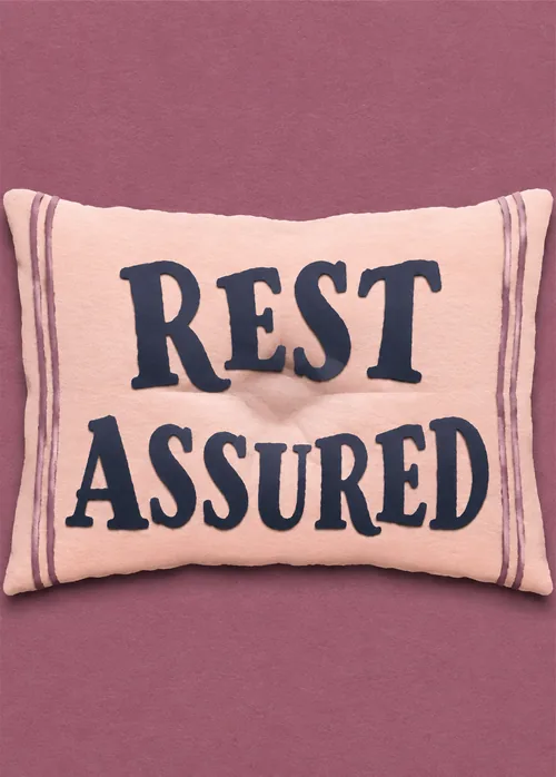 Blush pink pillow embroidered with Rest Assured against a plum background